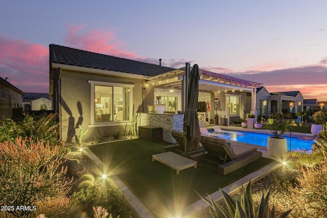 back of property at dusk with a patio, an outdoor pool, a tile roof, and stucco siding