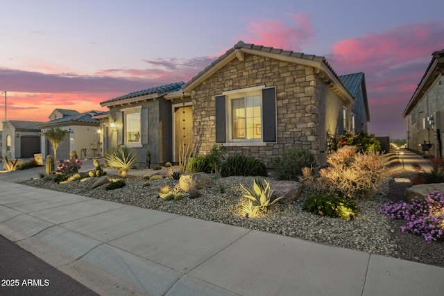 view of front of home with a garage, stone siding, driveway, and a tiled roof