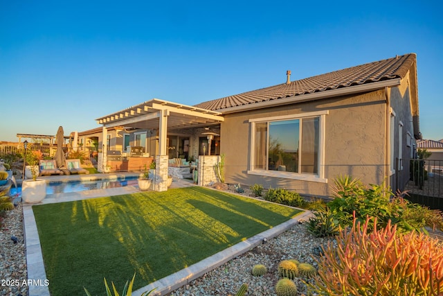 rear view of property featuring a fenced in pool, a tile roof, a yard, a pergola, and stucco siding