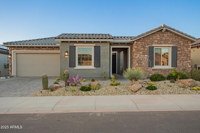 view of front of home with a garage, a tiled roof, decorative driveway, and stucco siding