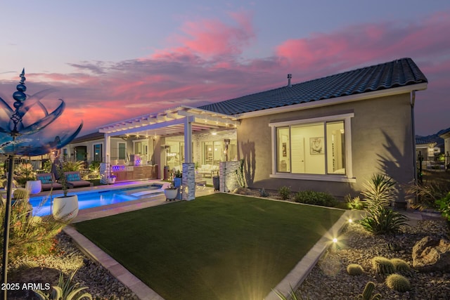 back of property at dusk with a tiled roof, stucco siding, a lawn, a pergola, and an outdoor living space