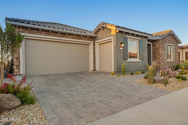 view of front of home with a garage, decorative driveway, a tile roof, and stone siding