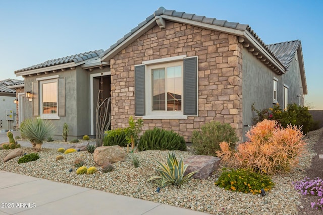 view of front facade with a tiled roof, stone siding, and stucco siding