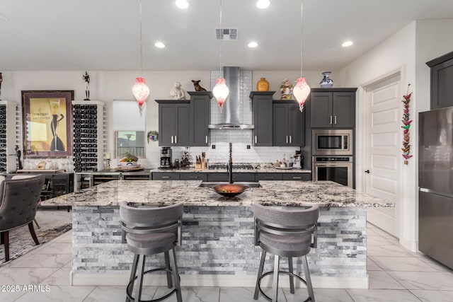 kitchen featuring marble finish floor, a breakfast bar area, backsplash, appliances with stainless steel finishes, and wall chimney range hood