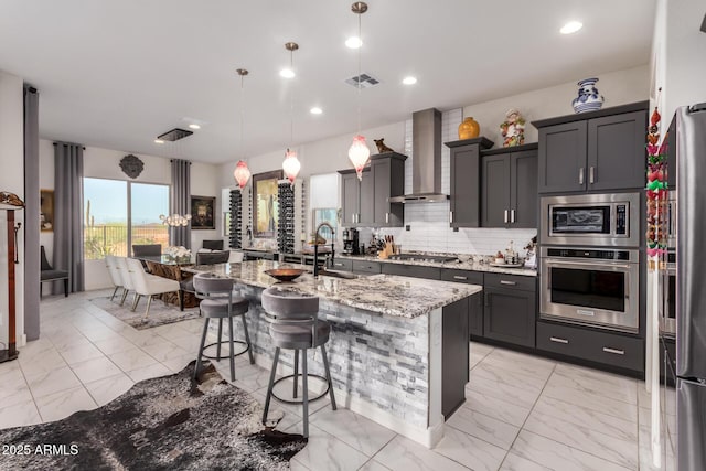 kitchen featuring wall chimney range hood, visible vents, stainless steel appliances, and marble finish floor