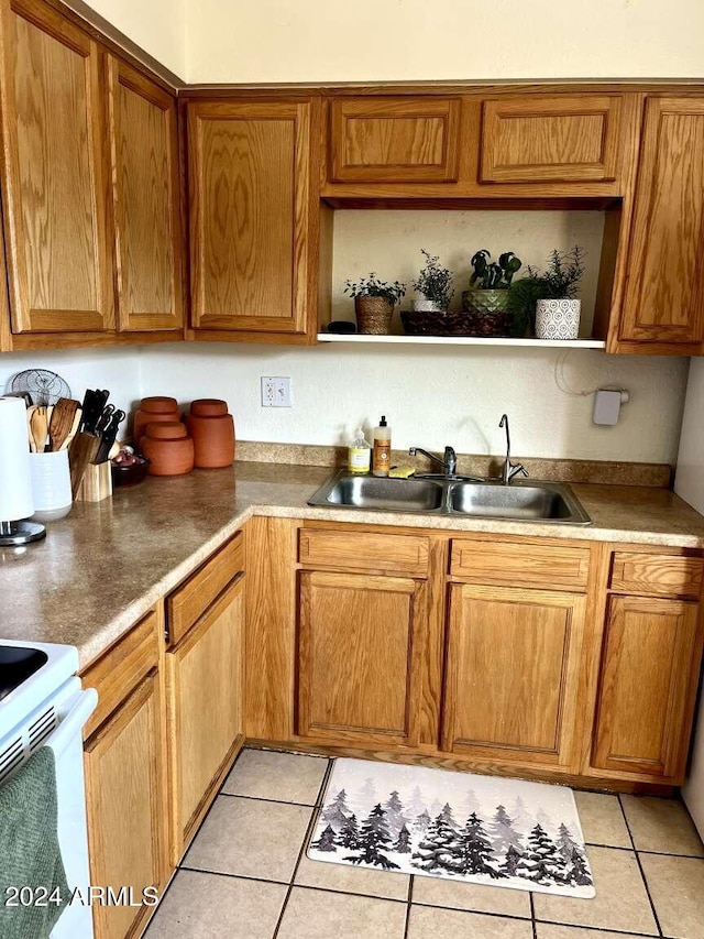 kitchen with white electric range oven, light tile patterned flooring, and sink