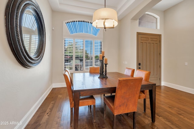 dining area with wood-type flooring, a high ceiling, and baseboards