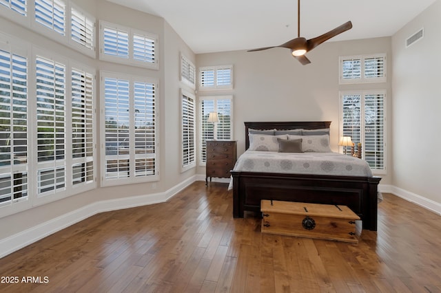 bedroom featuring hardwood / wood-style flooring, baseboards, a high ceiling, and visible vents