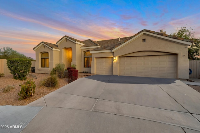 mediterranean / spanish home with an attached garage, fence, concrete driveway, and stucco siding