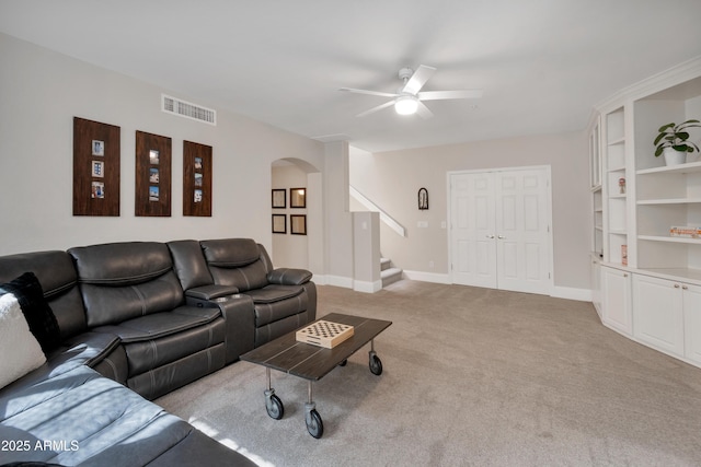 living room featuring arched walkways, light carpet, visible vents, baseboards, and stairway