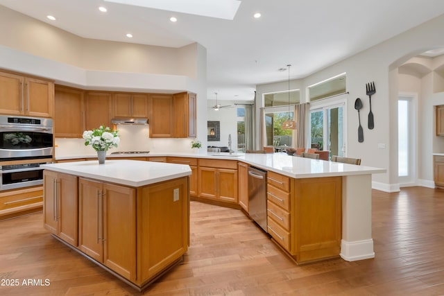 kitchen with under cabinet range hood, stainless steel appliances, a peninsula, a sink, and light countertops