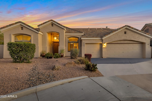 mediterranean / spanish home featuring a garage, concrete driveway, a tiled roof, and stucco siding