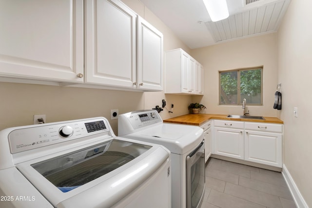 washroom with light tile patterned floors, a sink, baseboards, washer and dryer, and cabinet space