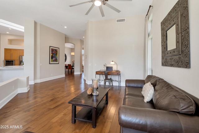 living room with arched walkways, wood-type flooring, visible vents, and baseboards