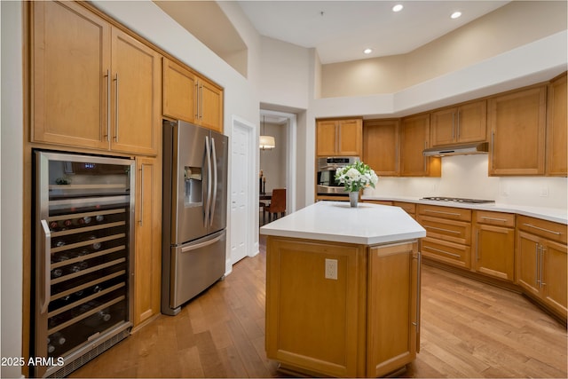 kitchen featuring light wood finished floors, stainless steel appliances, light countertops, beverage cooler, and under cabinet range hood