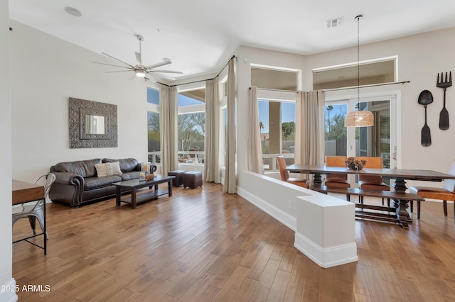 living area featuring a ceiling fan, visible vents, baseboards, and wood finished floors