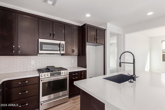 kitchen with dark brown cabinetry, sink, stainless steel appliances, tasteful backsplash, and light wood-type flooring