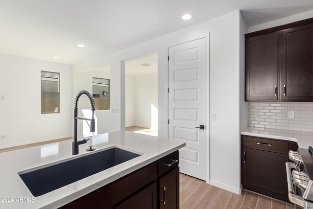 kitchen with light wood-type flooring, backsplash, dark brown cabinets, sink, and stainless steel range oven