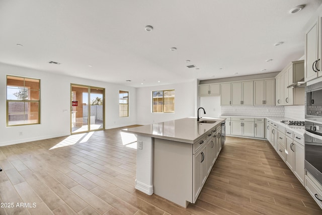 kitchen featuring sink, a kitchen island with sink, stainless steel appliances, tasteful backsplash, and light hardwood / wood-style floors