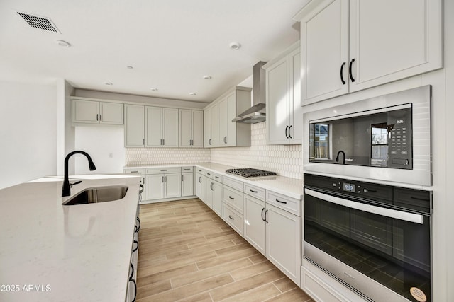 kitchen featuring wall chimney exhaust hood, sink, white cabinetry, light stone counters, and stainless steel appliances