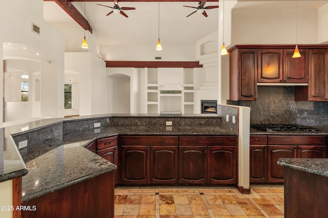 kitchen featuring stainless steel gas cooktop, decorative light fixtures, dark stone countertops, ceiling fan, and decorative backsplash