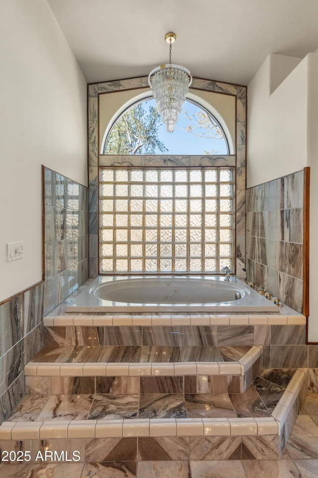 bathroom with tiled tub, a healthy amount of sunlight, and a notable chandelier