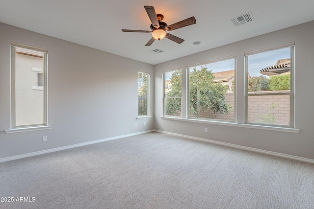 carpeted spare room featuring a healthy amount of sunlight, a ceiling fan, visible vents, and baseboards