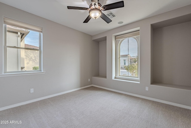 carpeted spare room with a healthy amount of sunlight, visible vents, ceiling fan, and baseboards