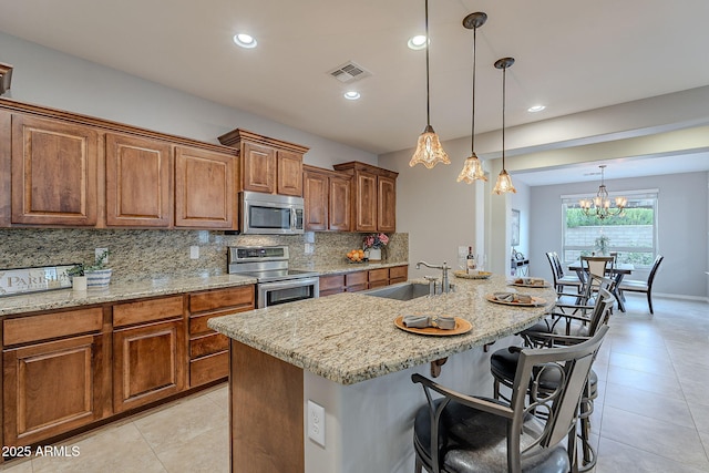 kitchen featuring a breakfast bar area, a kitchen island with sink, stainless steel appliances, a sink, and visible vents