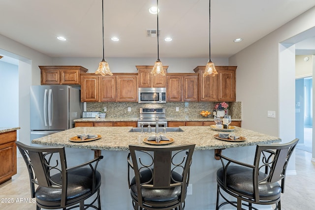 kitchen with appliances with stainless steel finishes, pendant lighting, brown cabinets, and a center island with sink