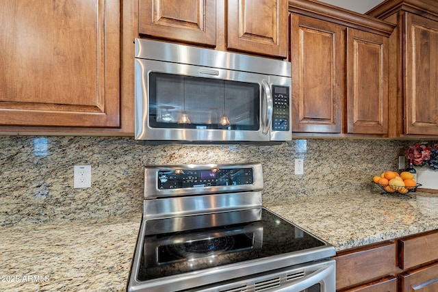 kitchen with appliances with stainless steel finishes, brown cabinetry, backsplash, and light stone countertops