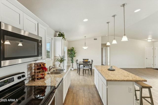 kitchen featuring light wood finished floors, vaulted ceiling, stainless steel appliances, white cabinetry, and a sink