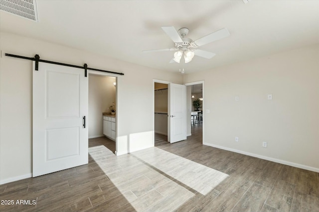 unfurnished bedroom featuring a barn door, wood finished floors, visible vents, and baseboards