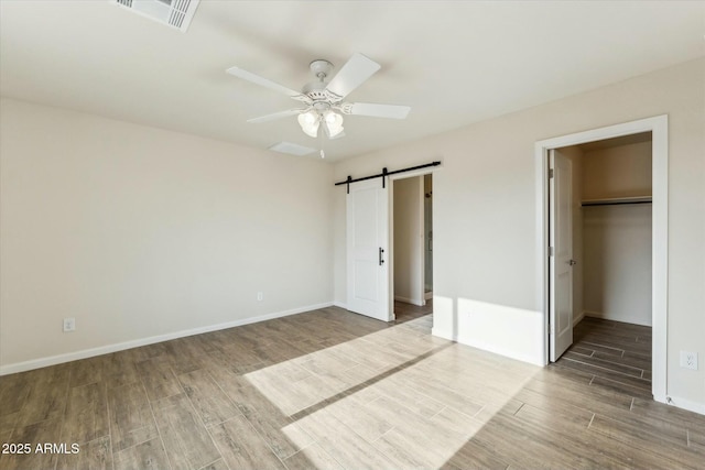 unfurnished bedroom featuring a barn door, visible vents, baseboards, and wood finish floors