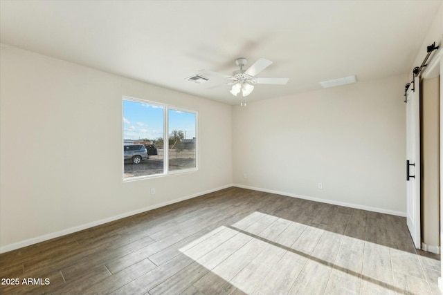 empty room with ceiling fan, a barn door, wood finished floors, visible vents, and baseboards