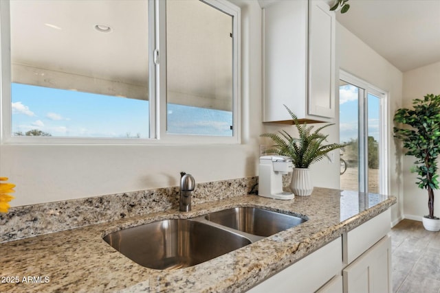 kitchen featuring white cabinets, a sink, light wood finished floors, and light stone countertops