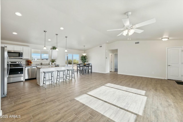 kitchen featuring a center island, visible vents, appliances with stainless steel finishes, light wood-type flooring, and a kitchen bar