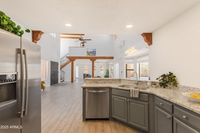 kitchen featuring light wood finished floors, light stone counters, appliances with stainless steel finishes, gray cabinets, and a sink