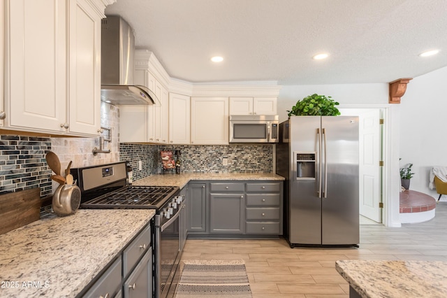 kitchen featuring gray cabinetry, stainless steel appliances, light wood-style floors, wall chimney range hood, and decorative backsplash