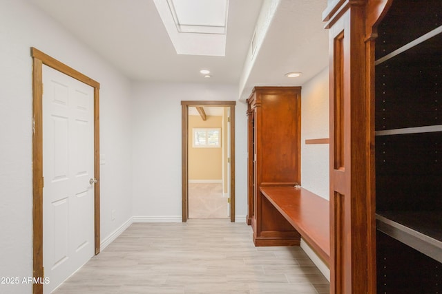 corridor featuring light wood-style floors, a skylight, baseboards, and recessed lighting