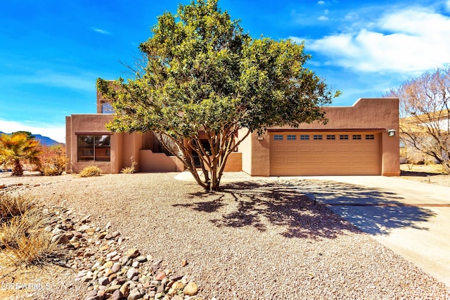 pueblo-style home featuring a garage, concrete driveway, and stucco siding