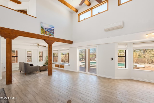 unfurnished living room with wood finished floors, a ceiling fan, baseboards, a wall mounted AC, and beamed ceiling