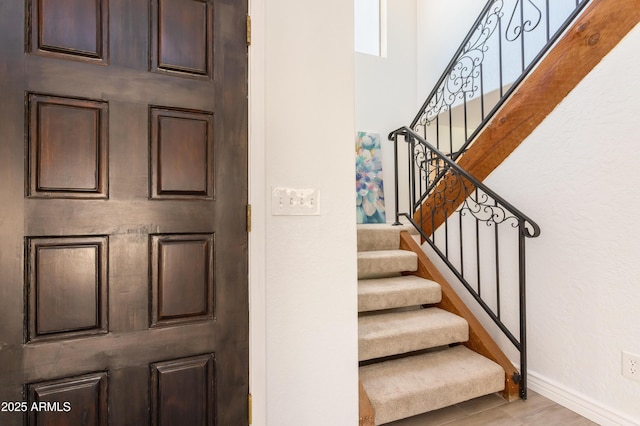 stairway featuring a high ceiling, baseboards, and wood finished floors