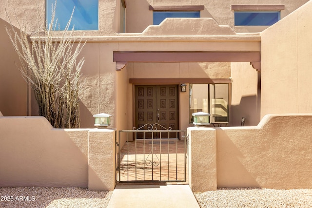 doorway to property featuring a gate, fence, and stucco siding