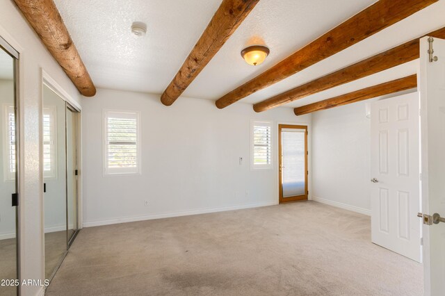 spare room with baseboards, light colored carpet, beam ceiling, and a healthy amount of sunlight