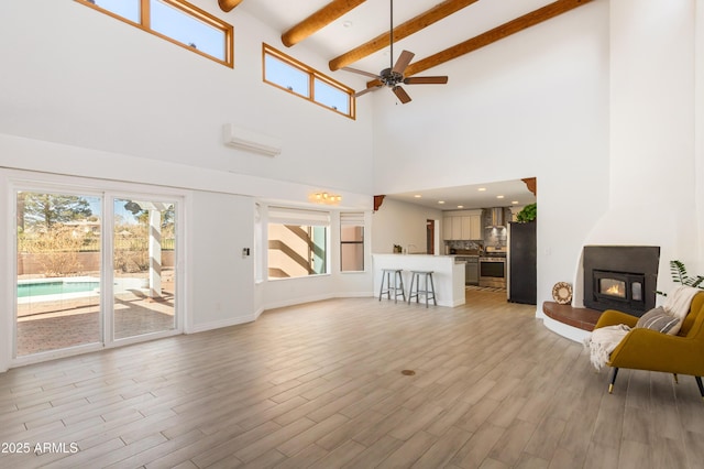 living room featuring ceiling fan, light wood finished floors, beamed ceiling, and a glass covered fireplace