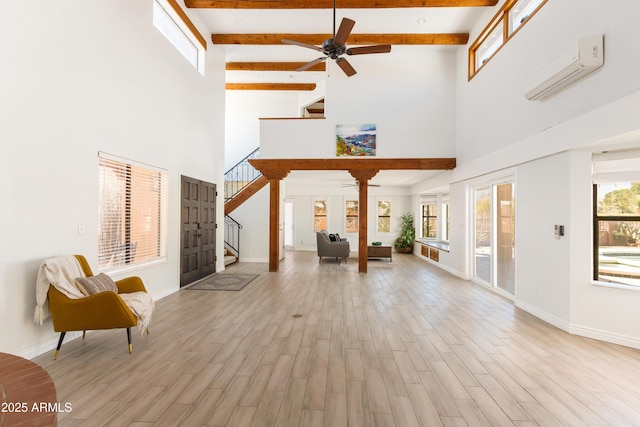 living area with beam ceiling, a wall unit AC, stairway, ceiling fan, and wood finished floors