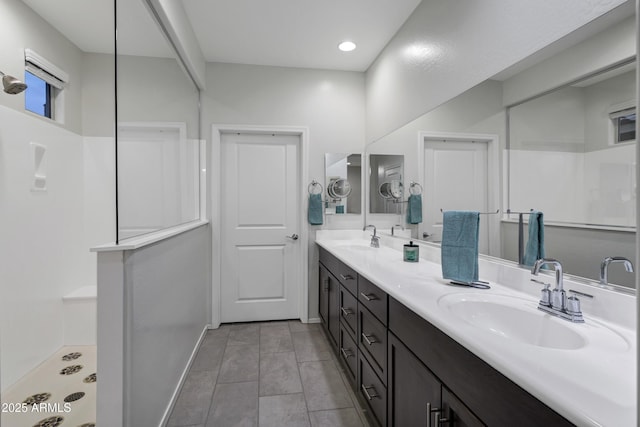 full bath featuring a walk in shower, double vanity, a sink, and baseboards