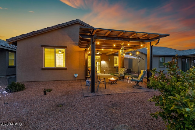 back of house at dusk featuring a patio area, a fire pit, a pergola, and stucco siding