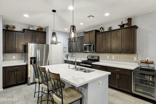 kitchen with beverage cooler, dark brown cabinetry, light countertops, appliances with stainless steel finishes, and a sink